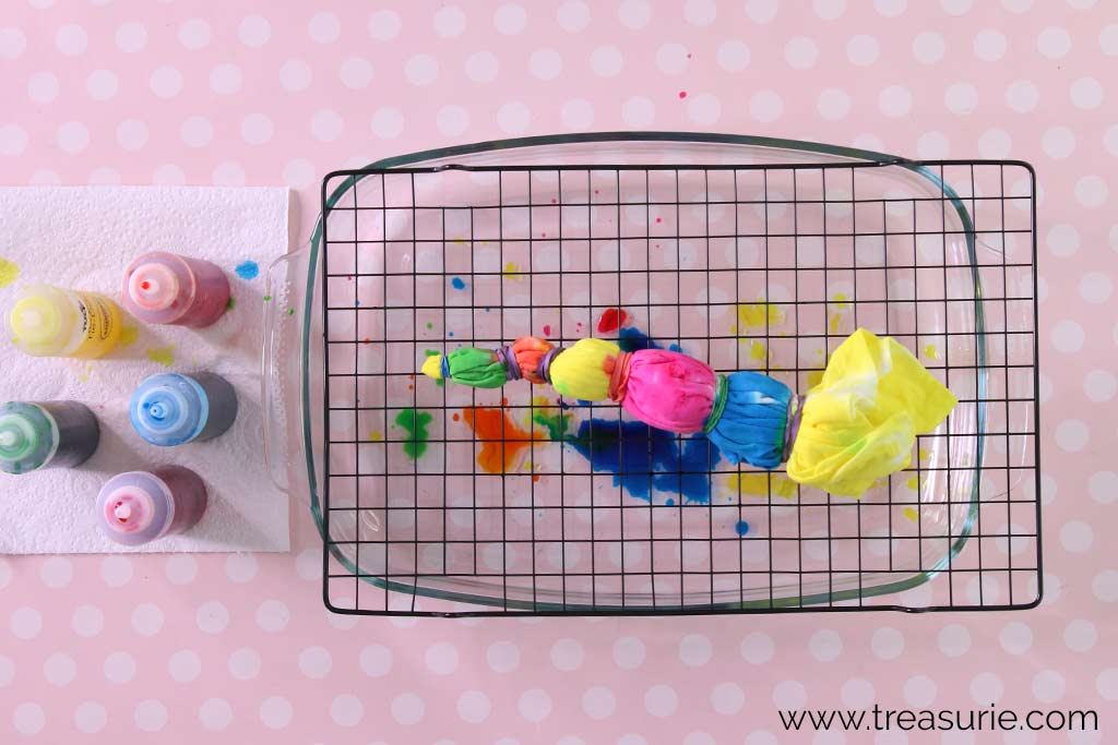 Top view of a rack with a shirt covered in dyes and bottles of liquid tie dye on the side